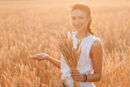 Woman holding sheaf of wheat ears at agricultural fieldの写真素材