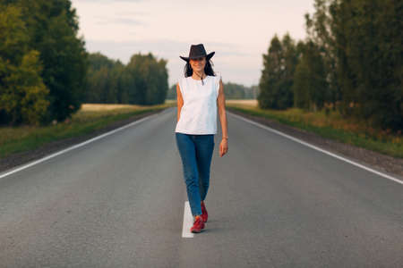 Woman with hat walking on the road dressed jeans