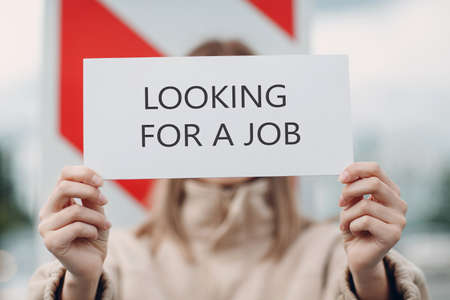 Young woman hold white paper poster in hand. Girl with white blank template sheet with inscription Looking for a job.の写真素材