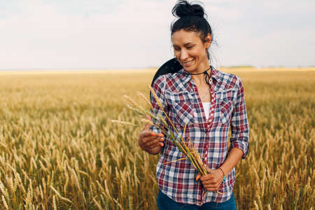 Woman american farmer with sheaf ears wearing cowboy hat, plaid shirt and jeans at wheat fieldの写真素材