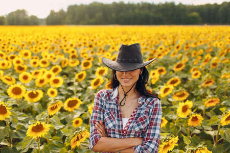 Young woman agronomist wearing cowboy hat, plaid shirt and jeans on sunflower field. Rich harvest concept.の写真素材