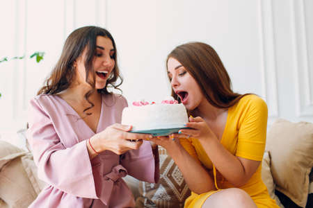 Women happy friends at home sit and eat white birthday cakeの写真素材