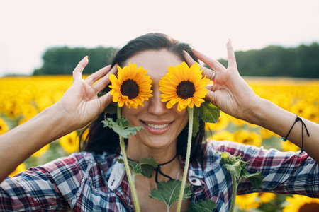 Portrait of a young woman in a shirt in the sunflower field hold eyes with sunflowers.の写真素材