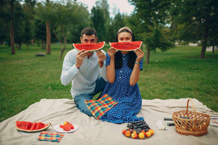 Young adult woman and man couple picnic at green grass meadow in park having fun and smile with watermelonの写真素材