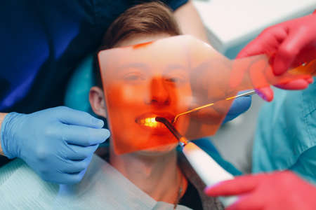 Dentistry. Dentist and patient. Light curing seal. UV dental lamp and orange protect glass.の写真素材
