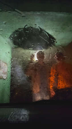 Two people with umbrella in the rain through car window at night.の写真素材