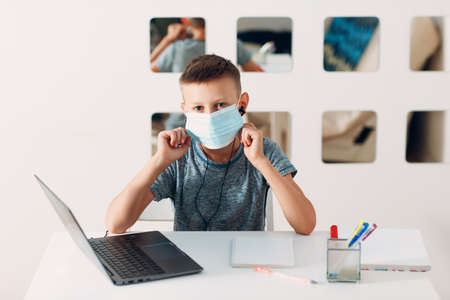 Young boy in headset sitting at table with laptop and medical face mask and preparing to school. Online education concept.の写真素材