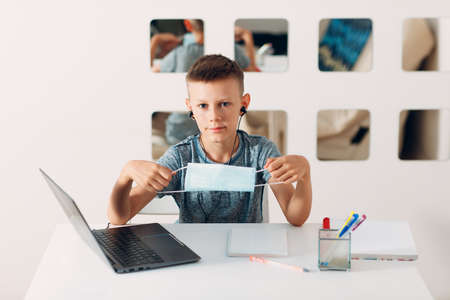 Young boy in headset sitting at table with laptop and medical face mask and preparing to school. Online education concept.の写真素材
