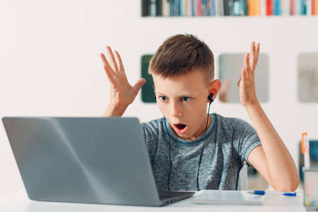 Young boy in headset sitting at table with laptop and preparing to school. Online education concept.の写真素材