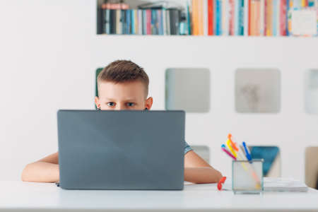 Young boy sitting at table with laptop and preparing to school. Online education concept.の写真素材