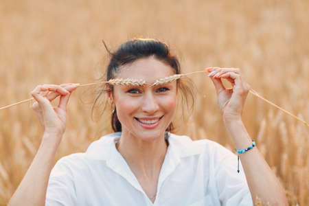 Portrait of a beautiful smiling brunette woman with ears of wheat on her eyebrowsの写真素材