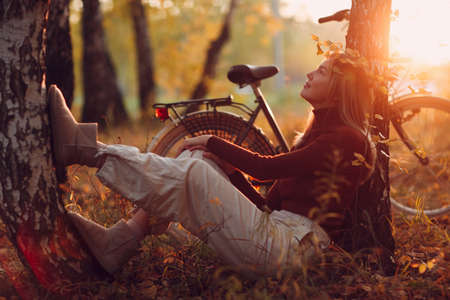 Happy active young woman sitting with vintage bicycle in autumn park at sunset