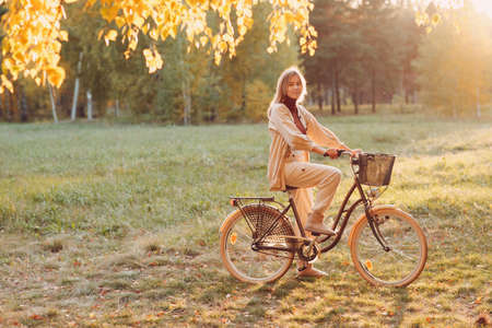 Happy active young woman riding bicycle in autumn parkの写真素材