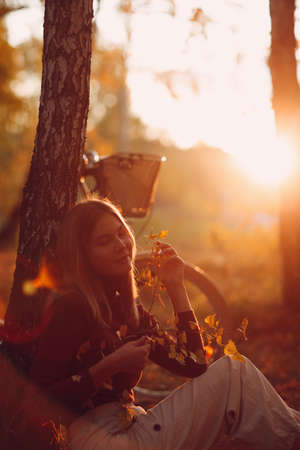 Happy active young woman sitting with vintage bicycle in autumn park at sunset