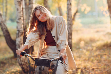 Happy smiling young woman riding vintage bicycle in autumn park at sunsetの写真素材