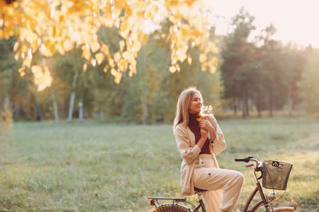 Happy active young woman holds fall leaves in hand ride bicycle in autumn parkの写真素材