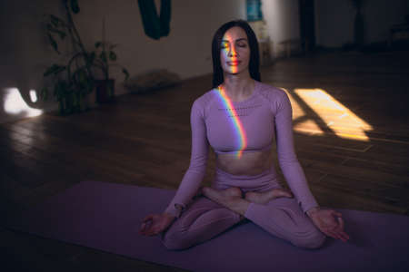 Woman practicing meditation and yoga with rainbow light on her body and faceの写真素材
