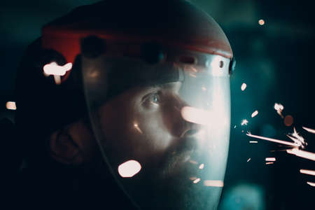 Man in transparent protective mask with flying sparks in darkness.の写真素材