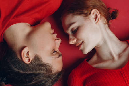 Two young people enjoying on the floor. Couple lovers man and woman lies on red background.