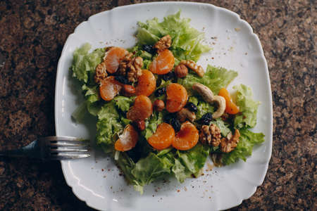 Close-up of tangerines, fresh lettuce salad and nuts top view