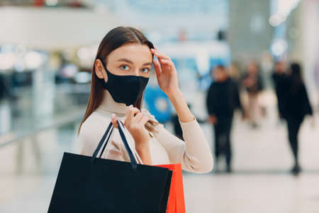 Young adult woman wearing protective medical face mask carrying paper shopping bags in hands at mall. Black fridayの写真素材