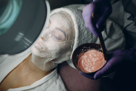 The process of preparation of pink alginate mask for face. Cup in the hands of a beautician.