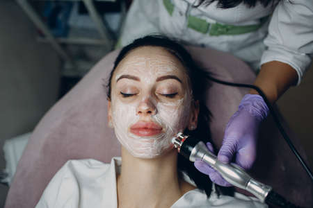 Young woman receiving electric RF lifting facial massage at beauty spa with electroporation equipment.の写真素材