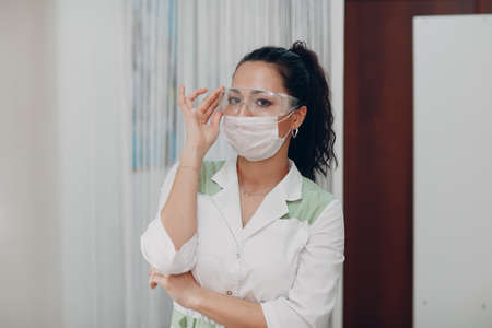 Young cute woman nurse or doctor in white coat and protective safety goggles glasses and a medical...