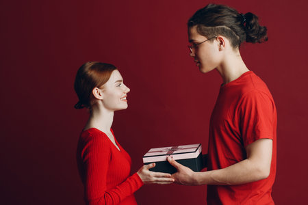 Valentine Day Gift. Happy Young Couple with Valentines Day Present isolated on red background.の写真素材