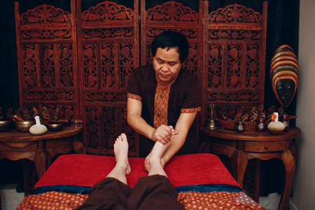 Thai man making classical feet thai massage procedure to young woman at beauty spaの写真素材