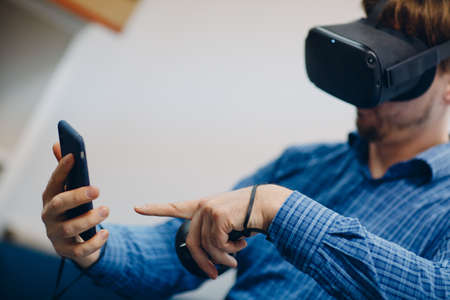 Young man in virtual reality goggles, vr glasses headset with joystick and mobile phone.の写真素材