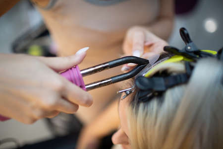 Hairdresser female making hair extensions to young woman with blonde hair in beauty salon. Professional hair extension.の写真素材