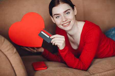 Pretty young woman at living room in home holding credit card in hand and smartphone with box, online shopping and marketing and deliveryの写真素材
