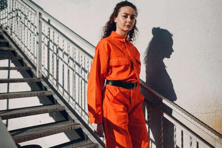Young brunette curly woman in orange suit. Female in colorful overalls portrait.の写真素材
