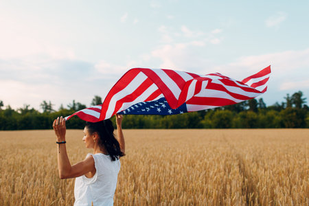 Woman with American flag in wheat field at sunset. 4th of July. Independence Day and Harvesting Concept.の写真素材
