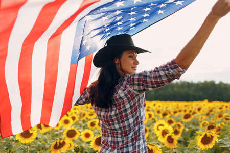 Young woman with American flag in the sunflower field. Harvest USA concept.の写真素材