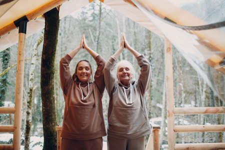 Woman senior and young relaxing at glamping camping tent outdoor. Women family elderly mother and young daughter doing yoga and meditation indoor. Modern zen-like vacation lifestyle concept.の写真素材