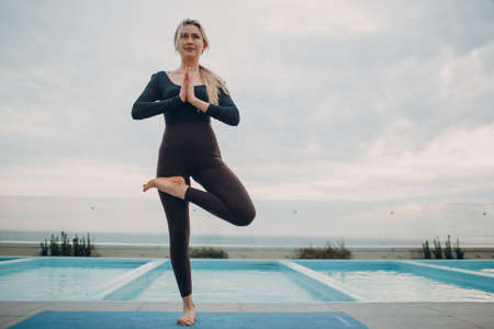 Caucasian woman practicing yoga at swimming poolの写真素材