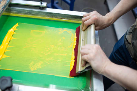 Serigraphy silk screen print process at clothes factory. Frame, squeegee and plastisol color paints.の写真素材