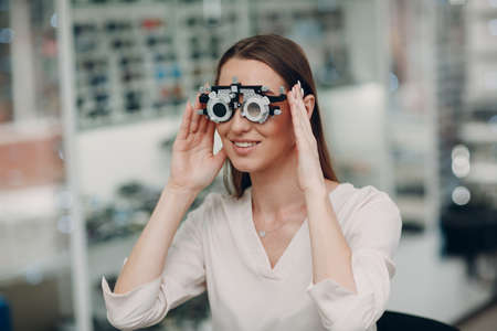 Portrait of happy young woman during eye exam with test goggles glasses at optometrist optician.の写真素材
