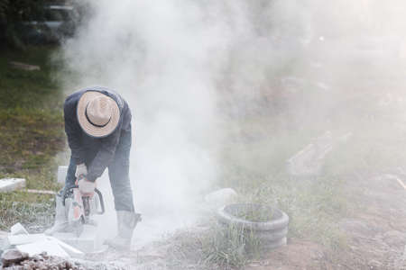 Worker mason cuts the sidewalk tile with circular saw while repairing sidewalk in city street.の写真素材