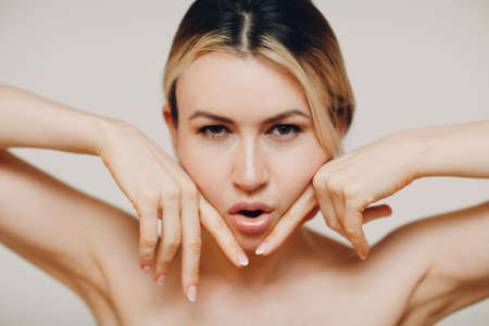 Woman making face yoga massage and rejuvenating exercises facebuilding with her handsの写真素材