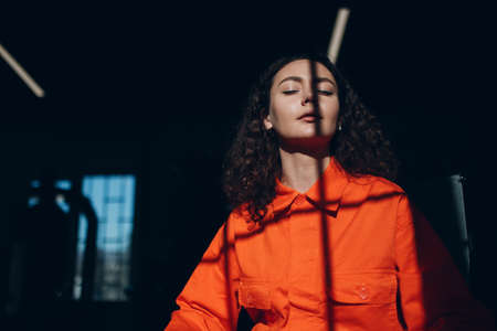Young woman in orange suit. Female in orange color overalls at jailの写真素材