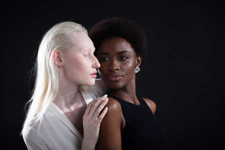Caucasian albino girl and african american young woman hugging on black background. Women friendship, love and relationships concept.の写真素材