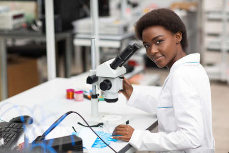 Scientist african american woman working in laboratory with electronic tech instruments and microscope. Research and development of electronic devices by color black woman.の写真素材