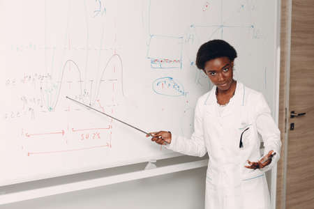 African American woman math teacher pointing at blackboard with pointer.