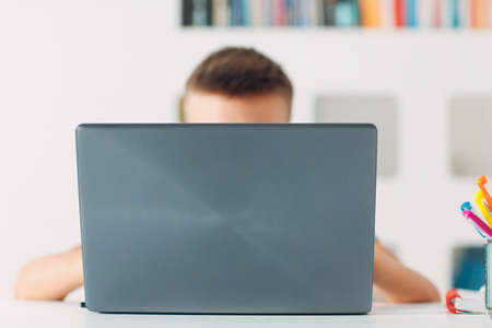 Young boy sitting at table with laptop and preparing to school. Online education concept