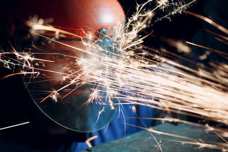 Worker in transparent protective mask works on metal with circular grinder saw. Sparks and faceの写真素材