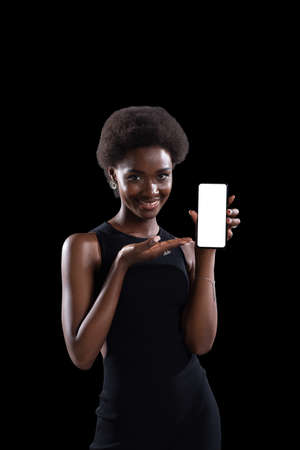 Smiling african american black woman pointing on empty template mobile phone white screen with copy space isolatedの写真素材