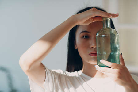 Asian young adult woman hold green glass bottle front face with day sunlight indoorの写真素材